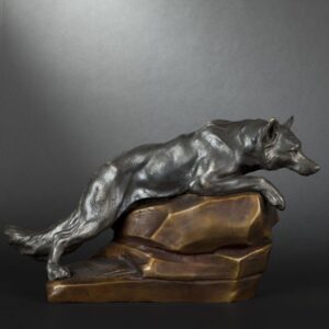 Photographie d'une statuette de loup à l’affût, en métal à patine argentée, sur un rocher à patine dorée.